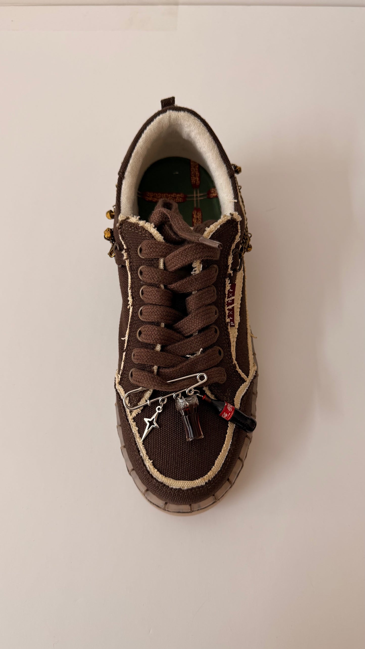 Coke, Obviously, brooch pin fastened to the laces of a brown canvas sneaker