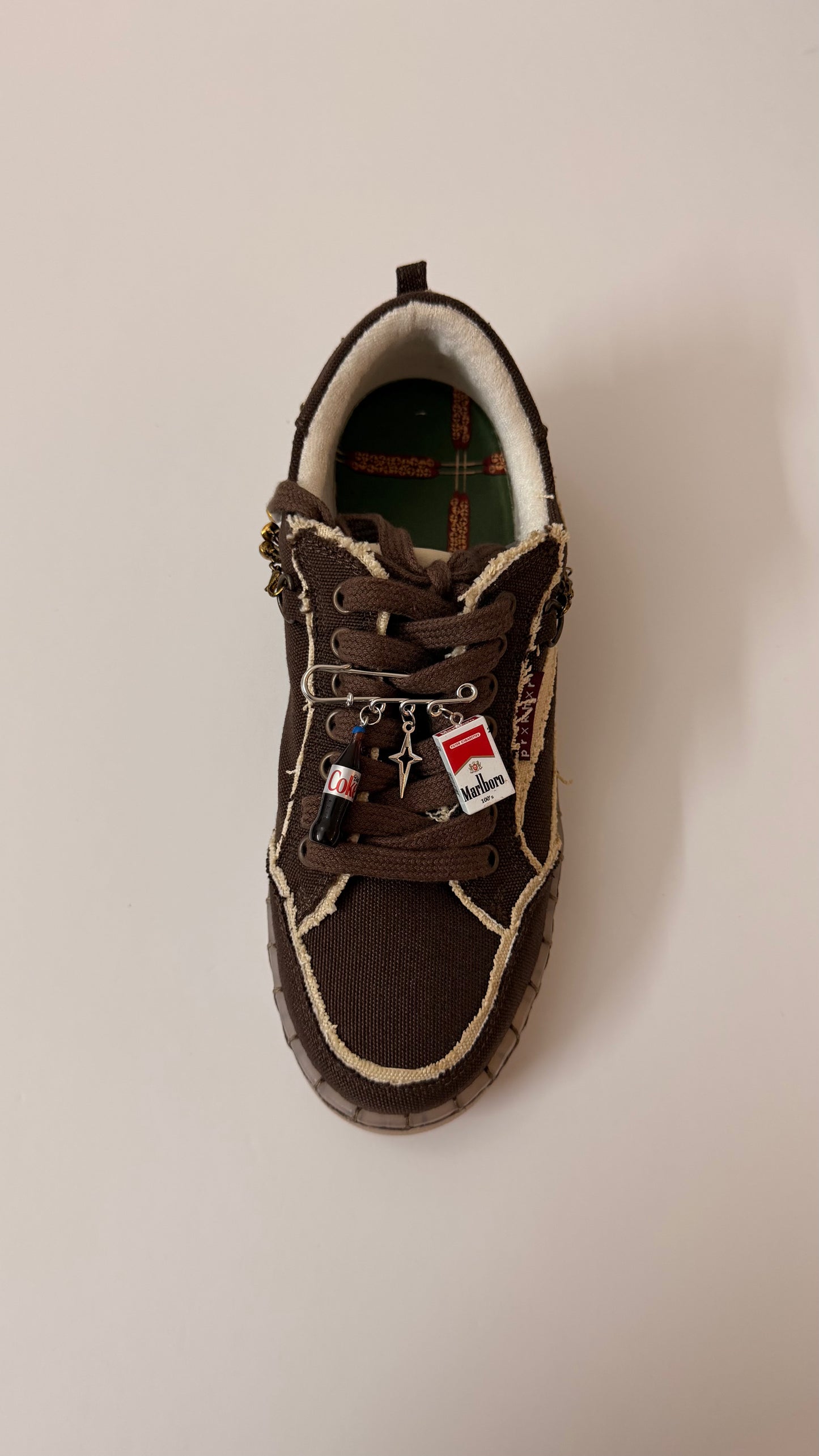 Coke & Smoke, brooch pin fastened to the laces of a brown canvas sneaker