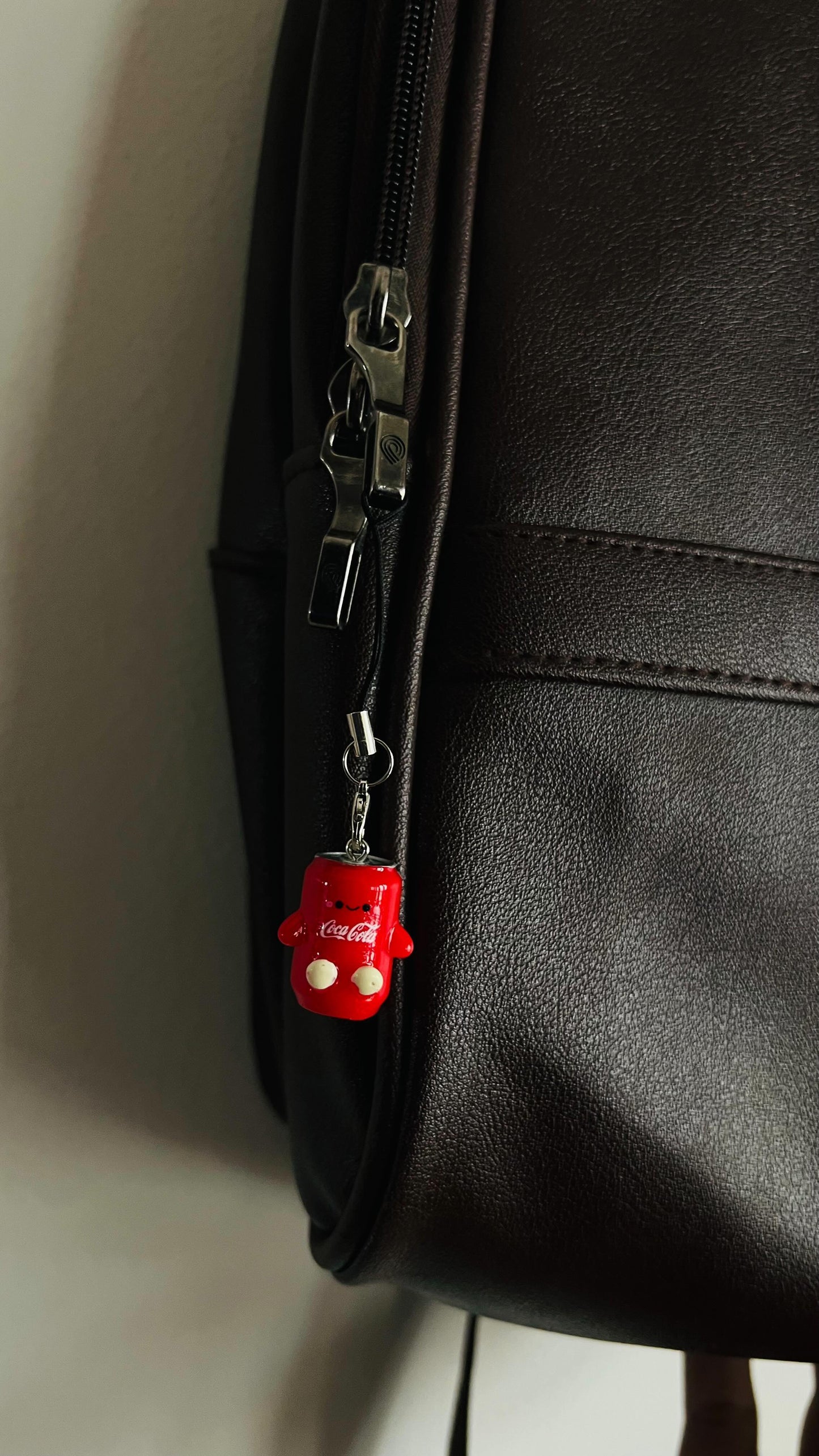 Red Coca-Cola character figurine charm clipped to a dark brown bag zipper