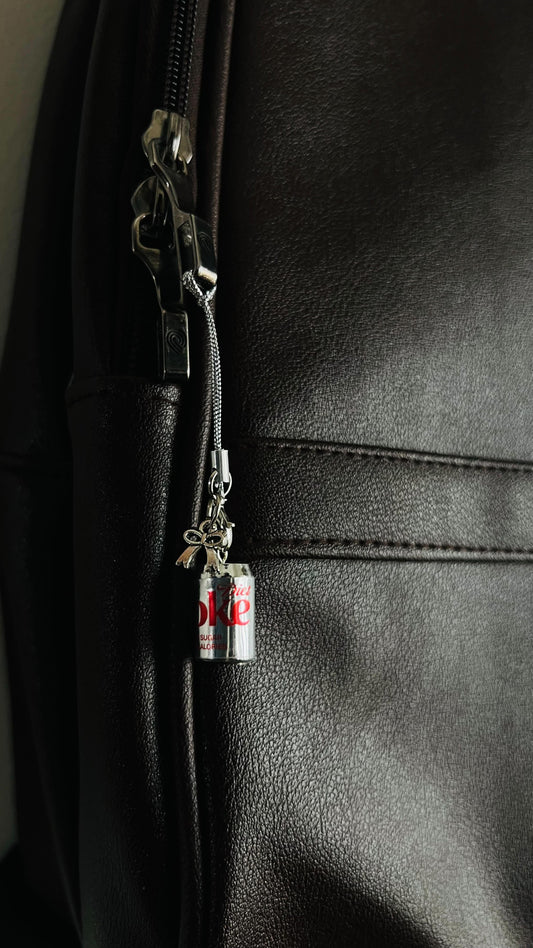 Metallic Diet Coke can charm with silver bow on a phone strap, hanging on a dark brown bag