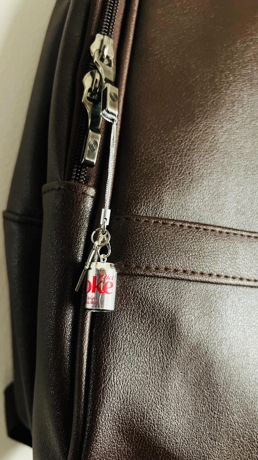 Metallic Diet Coke can charm clipped to a dark brown backpack zipper