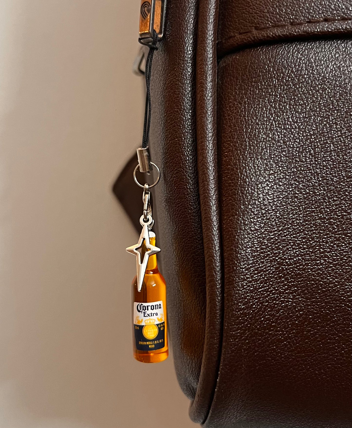 Corona Extra mini bottle phone charm with silver star on a black strap, dark brown bag