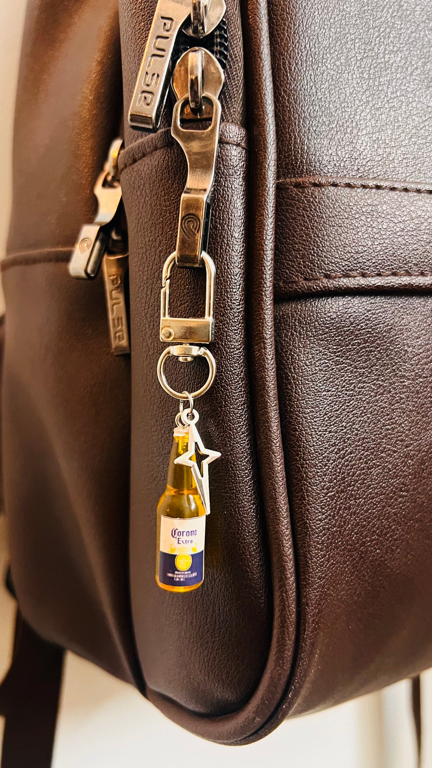 Mini Corona Extra bottle bag charm with silver star on a clasp, on a brown leather backpack