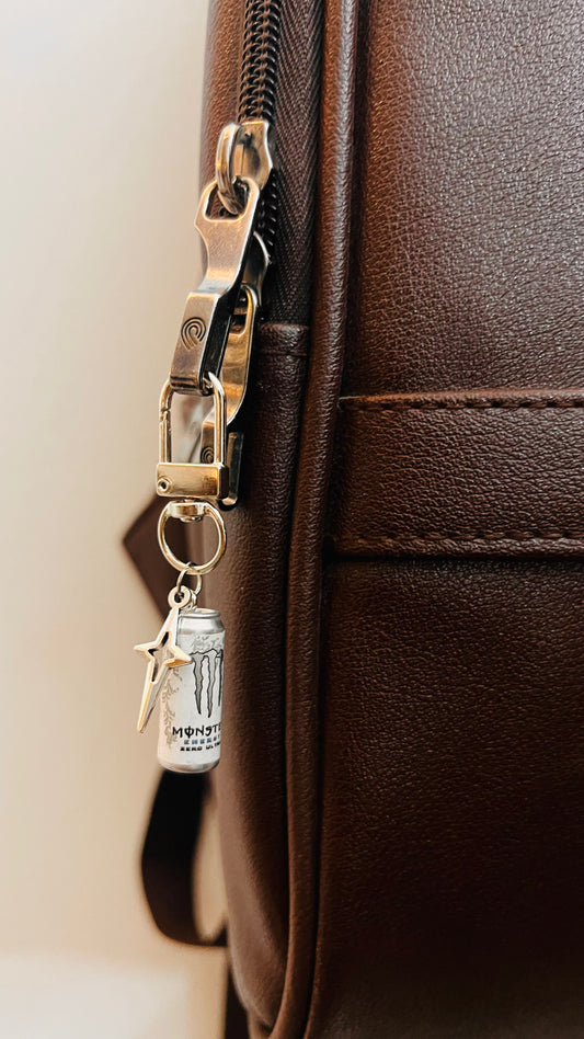 White Monster Energy can charm with silver star on a D-hook clasp, brown leather backpack