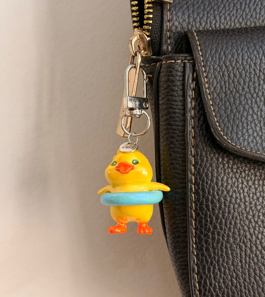 Pool Party Duck, a yellow duck in a pale blue swim ring clipped to a black leather handbag zip.