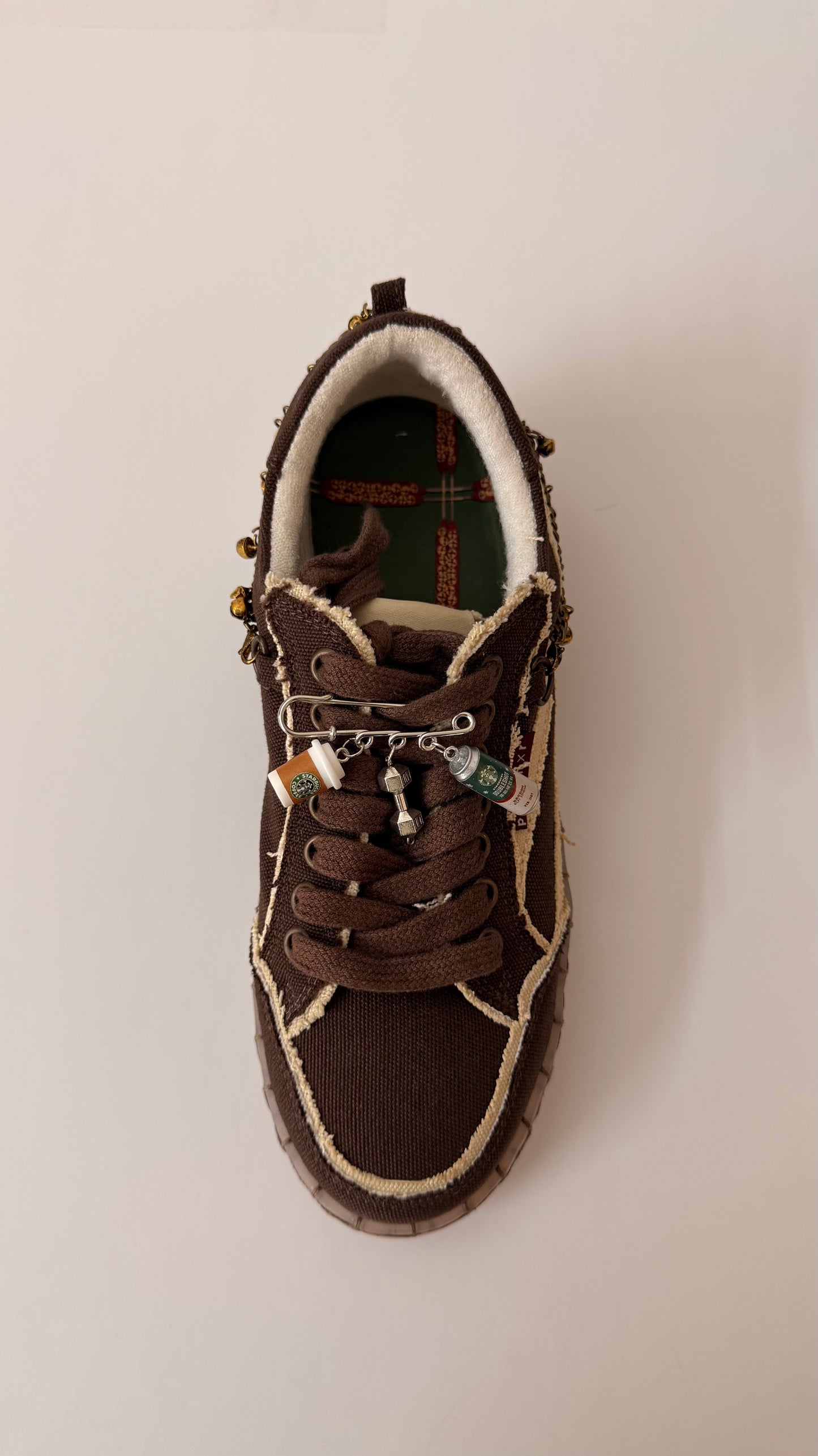 Pre-Workout Charm, brooch pin fastened to the laces of a brown canvas sneaker