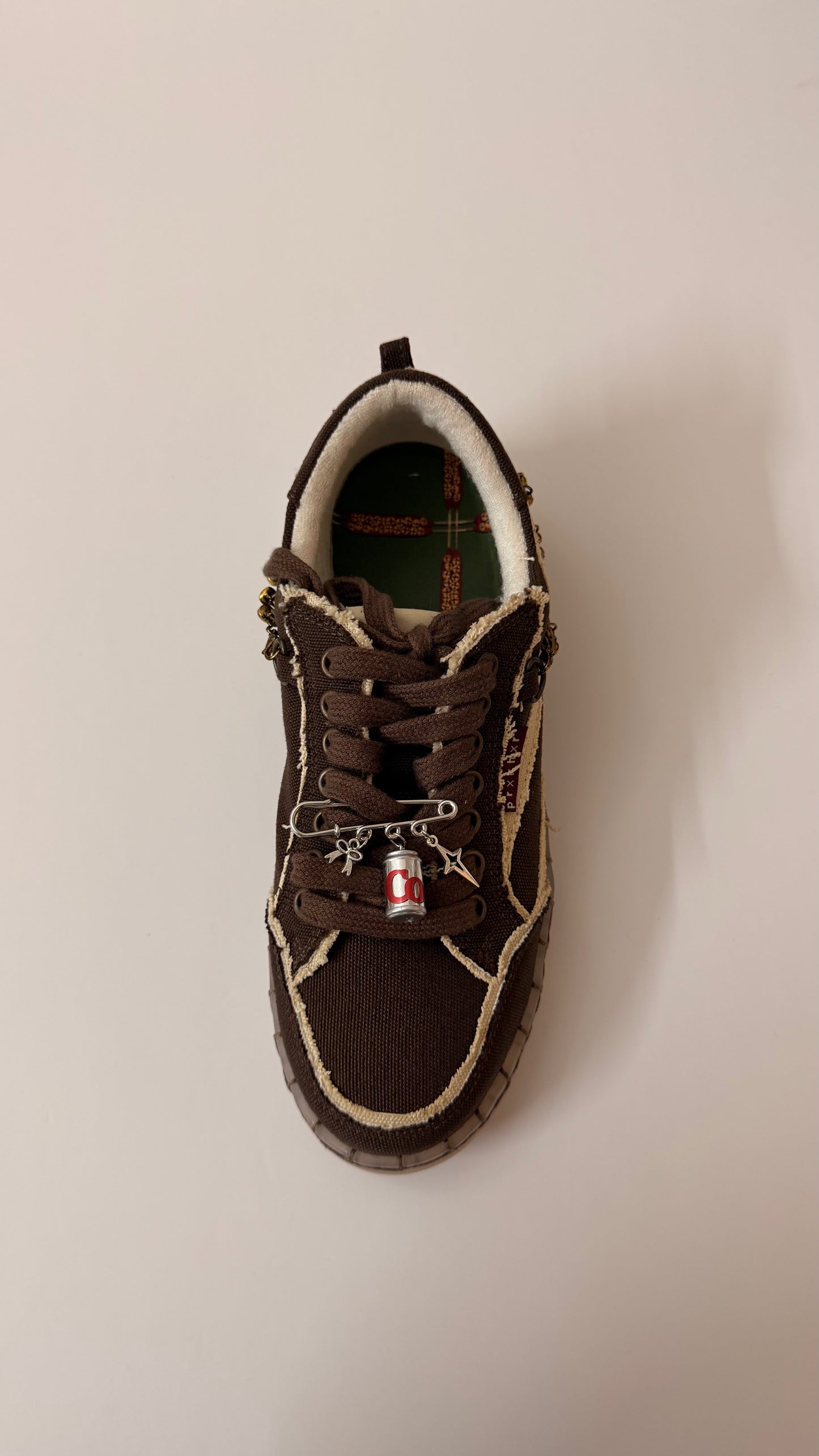 The Pop Charm, brooch pin fastened to the laces of a brown canvas sneaker