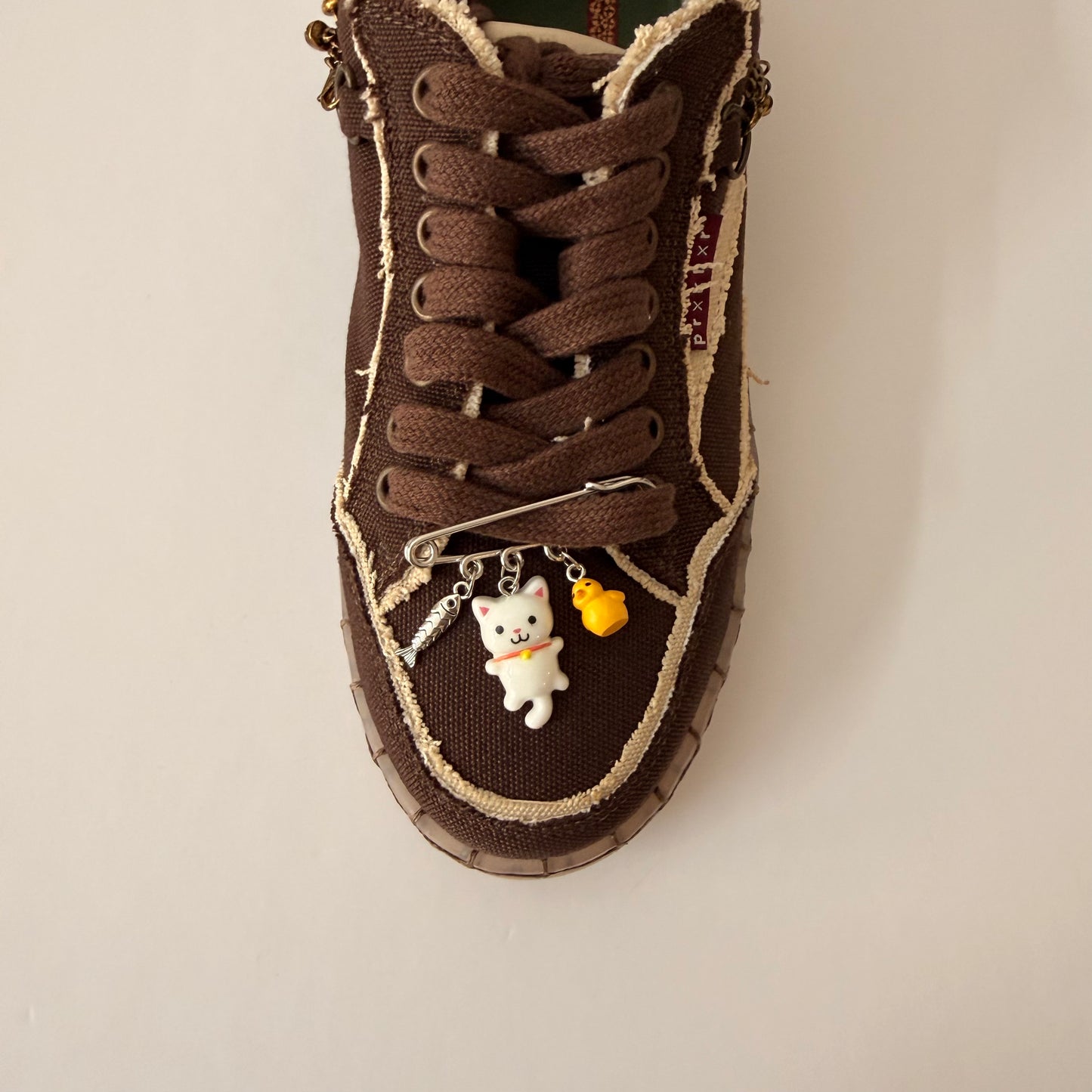 White Cat Charm, brooch pin fastened to the laces of a brown canvas sneaker