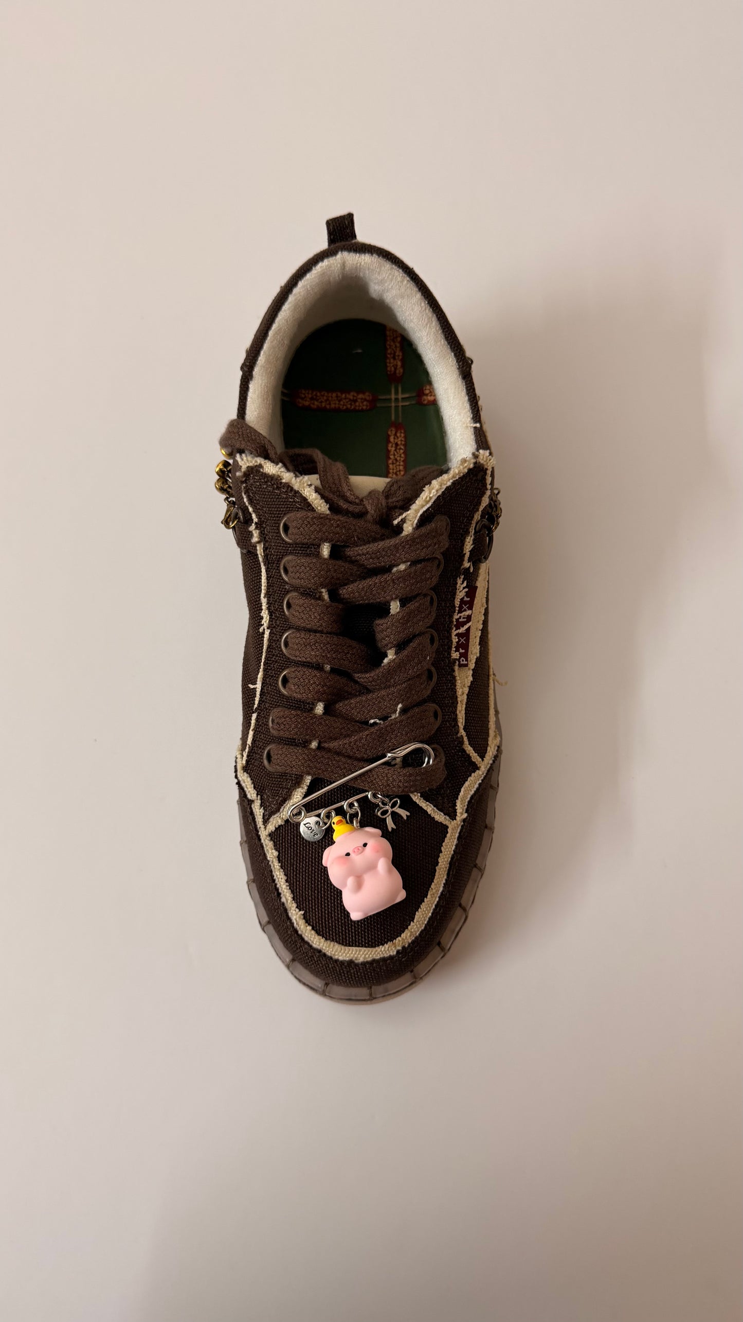 Oink Oink Charm, brooch pin fastened to the laces of a brown canvas sneaker