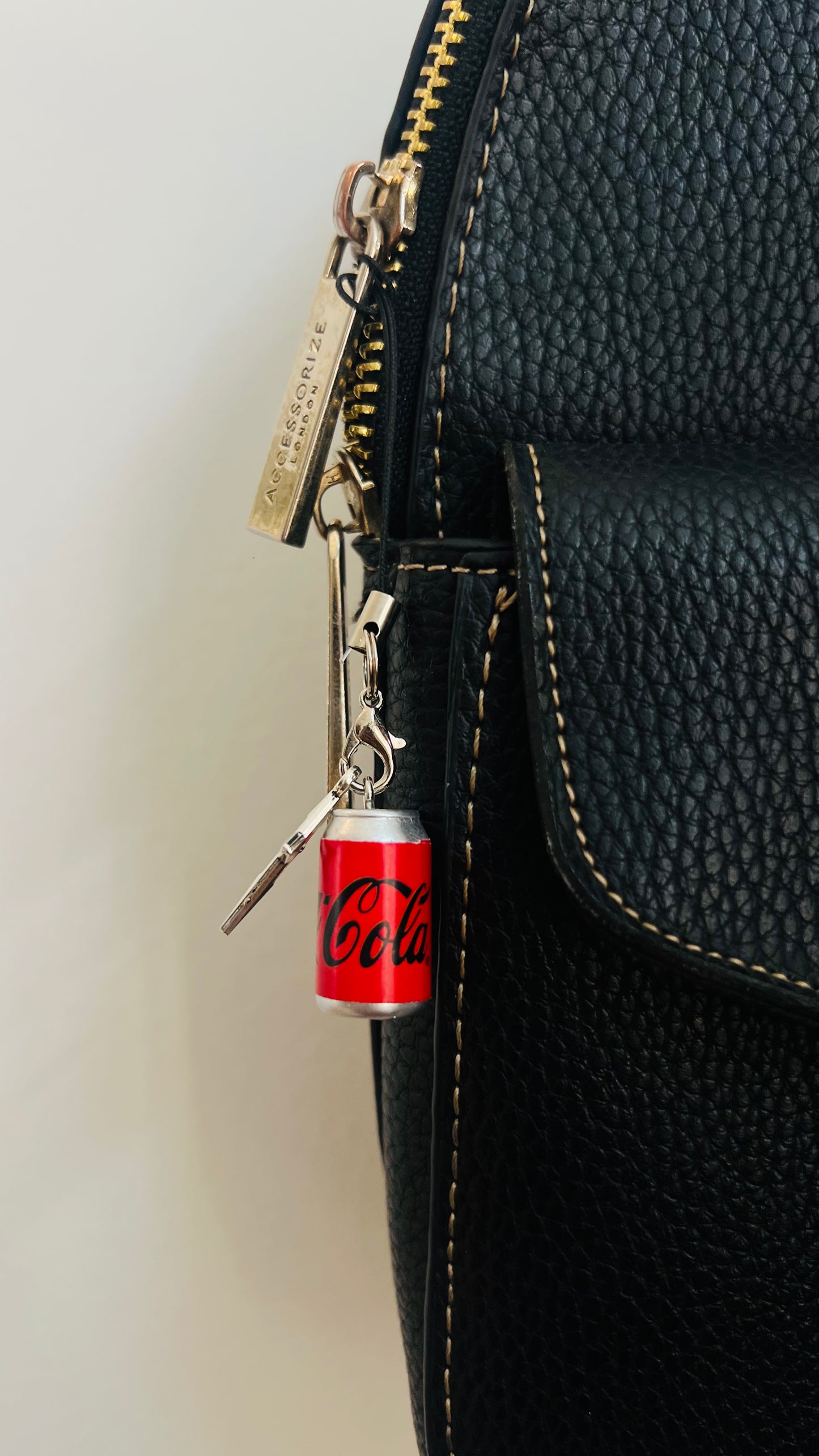 Red Coca-Cola can charm with a silver star on a phone strap, clipped to a black bag