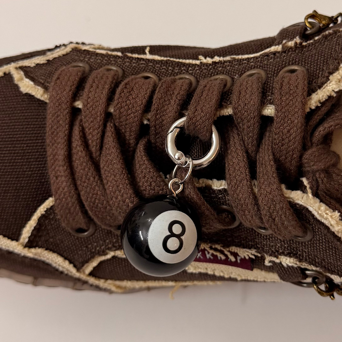 8Ball Shoe Charm, glossy black 8 ball charm on the laces of a brown canvas sneaker
