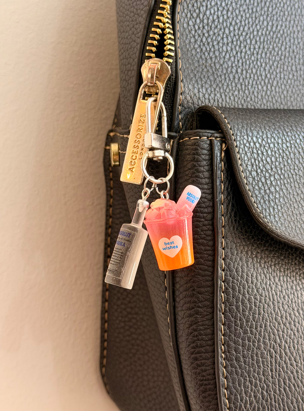 Absolut Orange Cocktail Bag Charm, a miniature clear Absolut vodka bottle with an orange cocktail cup clipped to a black leather handbag zip.