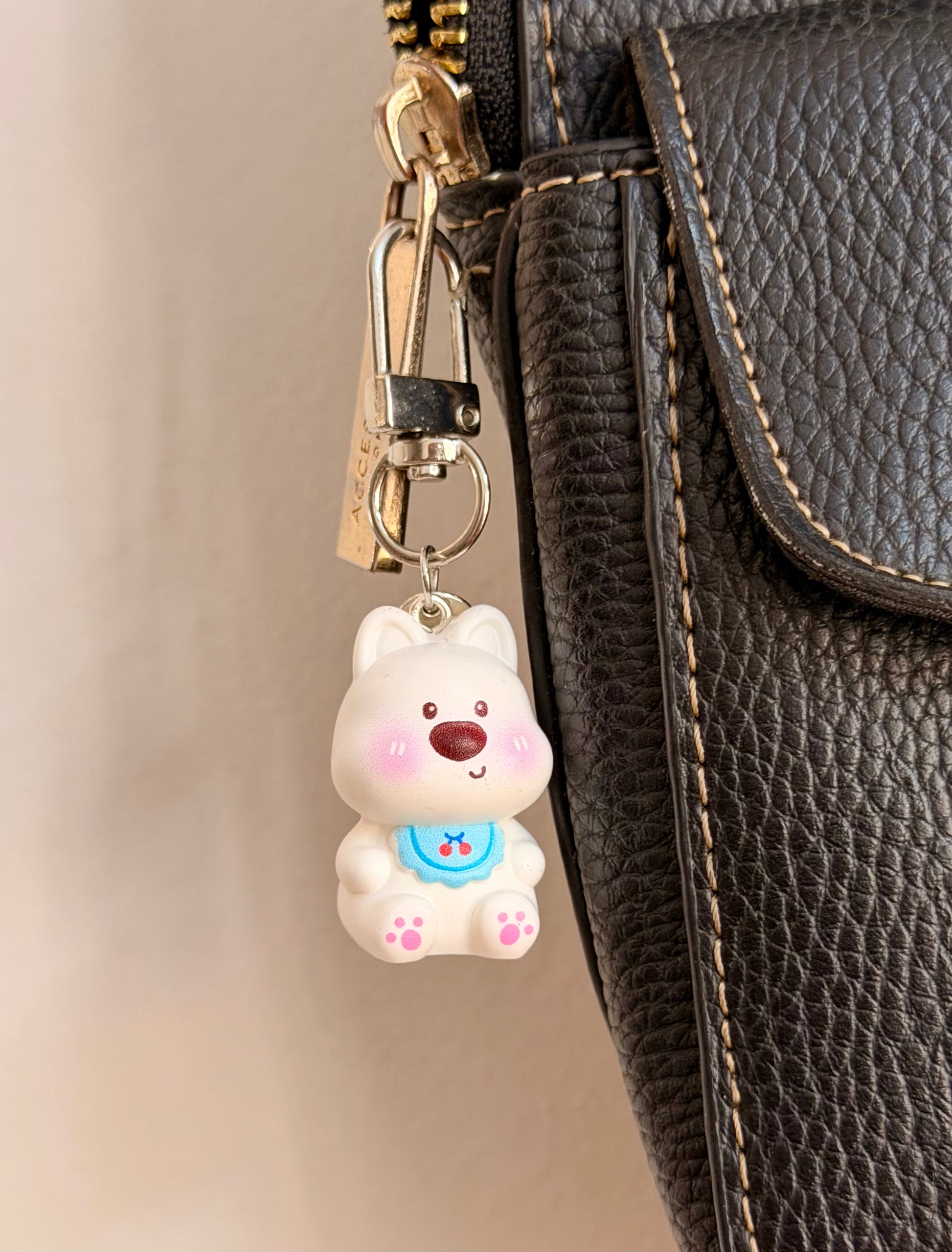 Bibbidi Bobbidi Boo, a white puppy in a blue bib patterned with red cherries clipped to a black leather handbag zip.