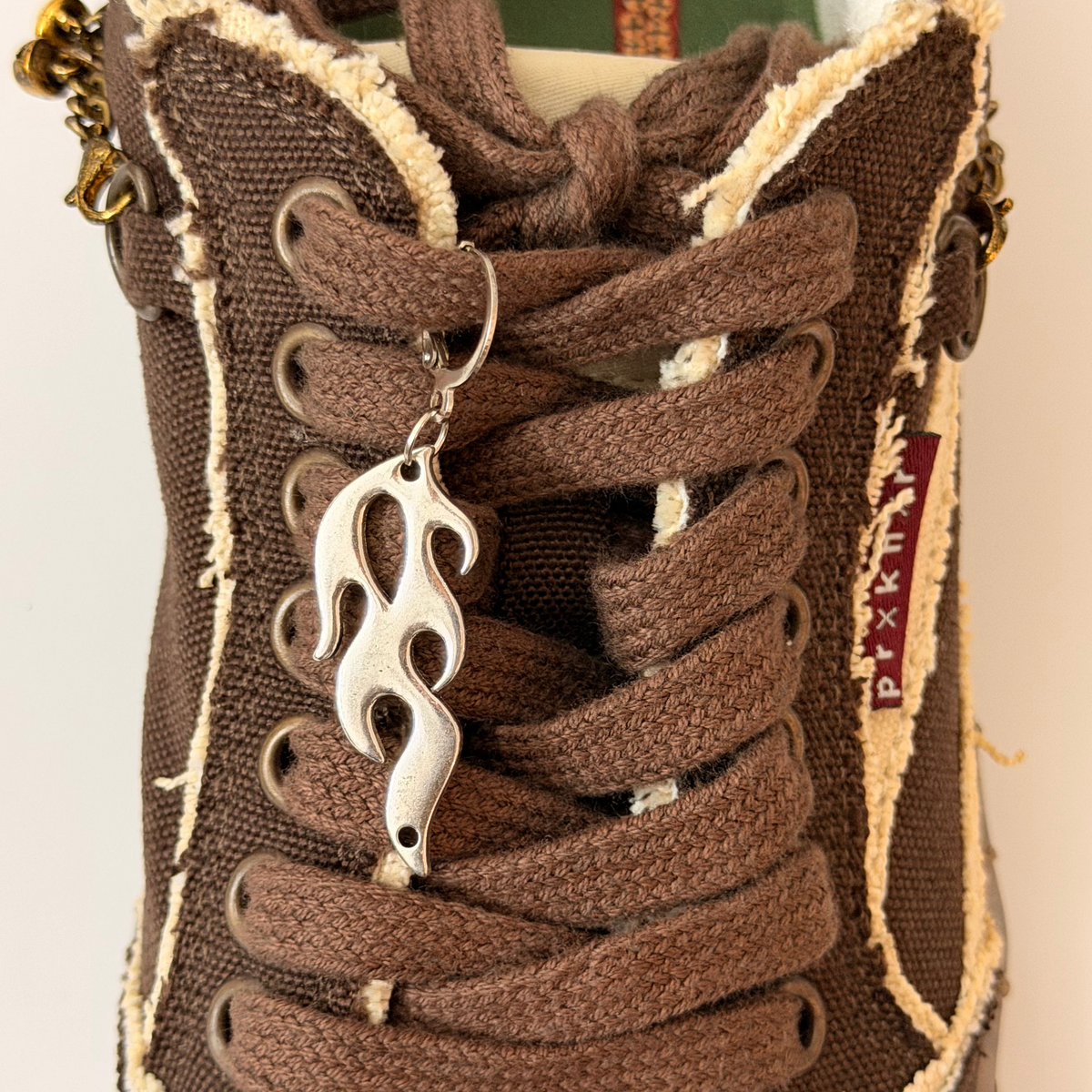 Blaze Shoe Charm, silver racing flame charm on the laces of a brown canvas sneaker