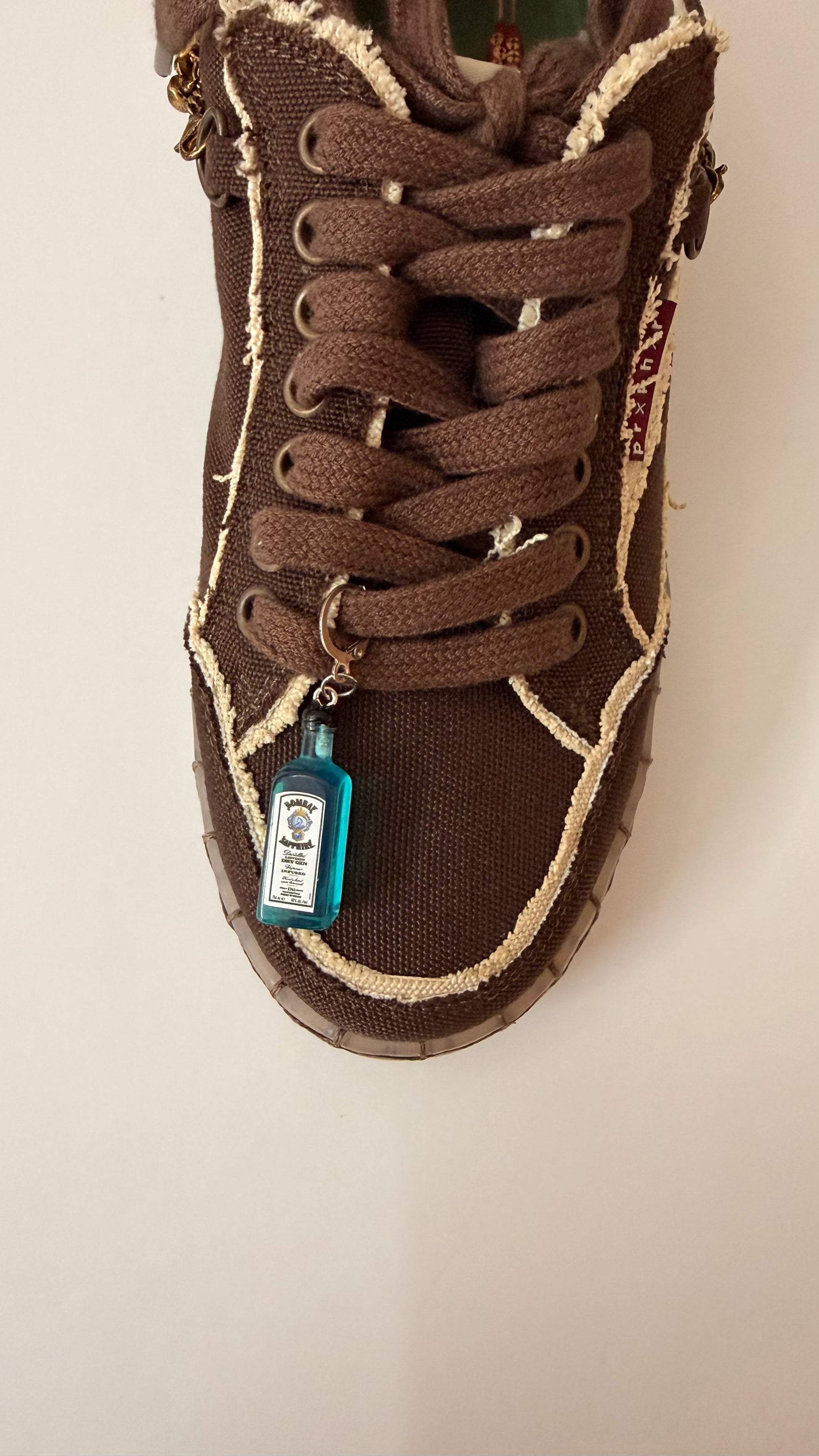 Bombay Sapphire Shoe Charm, mini blue Bombay Sapphire gin bottle charm on the laces of a brown canvas sneaker