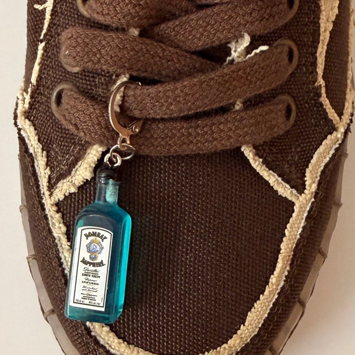 Bombay Sapphire Shoe Charm, mini blue Bombay Sapphire gin bottle charm on the laces of a brown canvas sneaker
