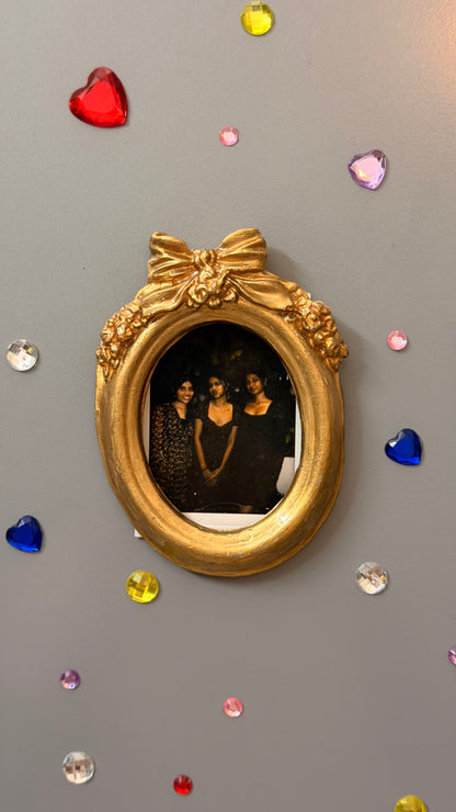 Bow and Blooms Magnetic Frame, gold concrete oval frame holding a photo, magnetised to a fridge door