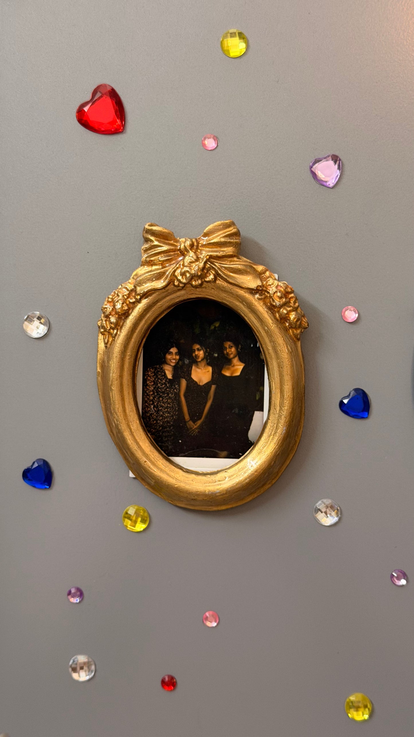 Bow and Blooms Magnetic Frame, gold concrete oval frame holding a photo of three friends on a fridge door
