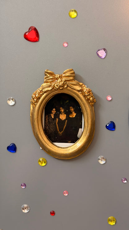 Bow and Blooms Magnetic Frame, gold concrete oval frame holding a photo of three friends on a fridge door