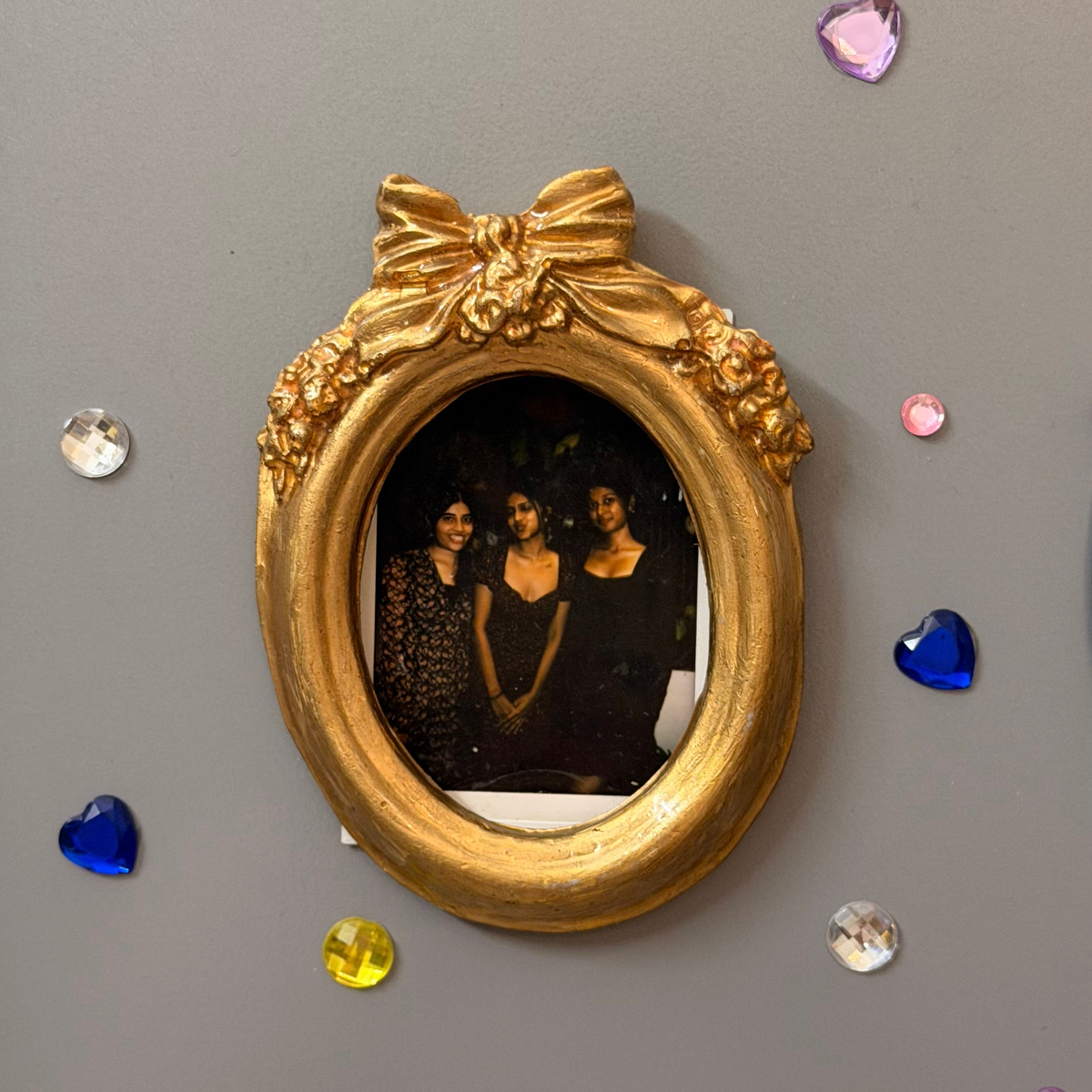 Bow and Blooms Magnetic Frame, gold concrete oval frame holding a photo of three friends on a fridge door