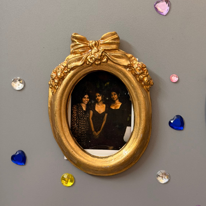 Bow and Blooms Magnetic Frame, gold concrete oval frame holding a photo of three friends on a fridge door