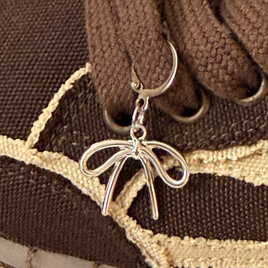 Ribbon Bow Shoe Charm, puffy silver bow charm with wavy tails on the laces of a brown canvas sneaker