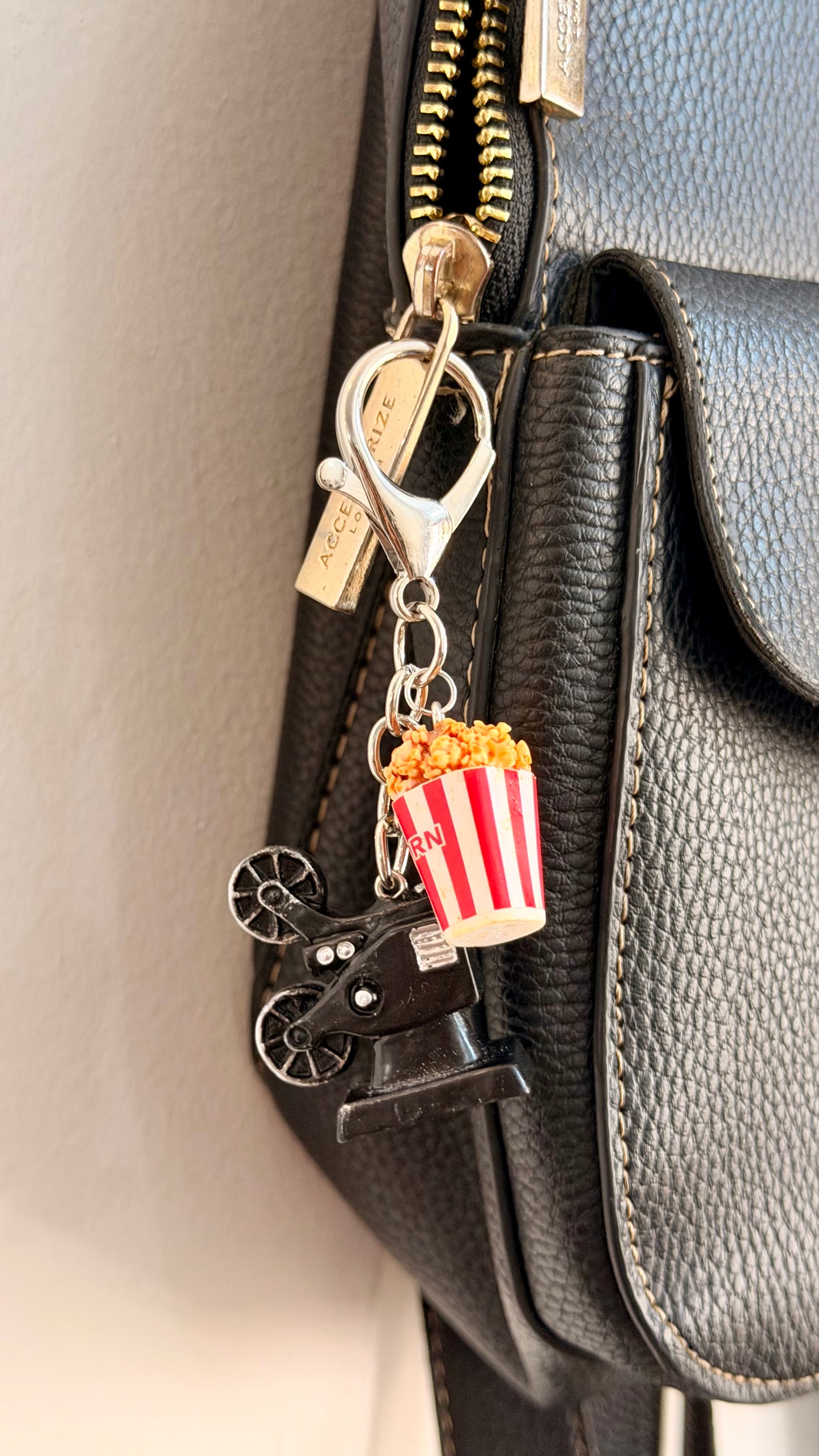 Certified Movie Buff, a vintage film projector with a striped popcorn box clipped to a black leather handbag zip.