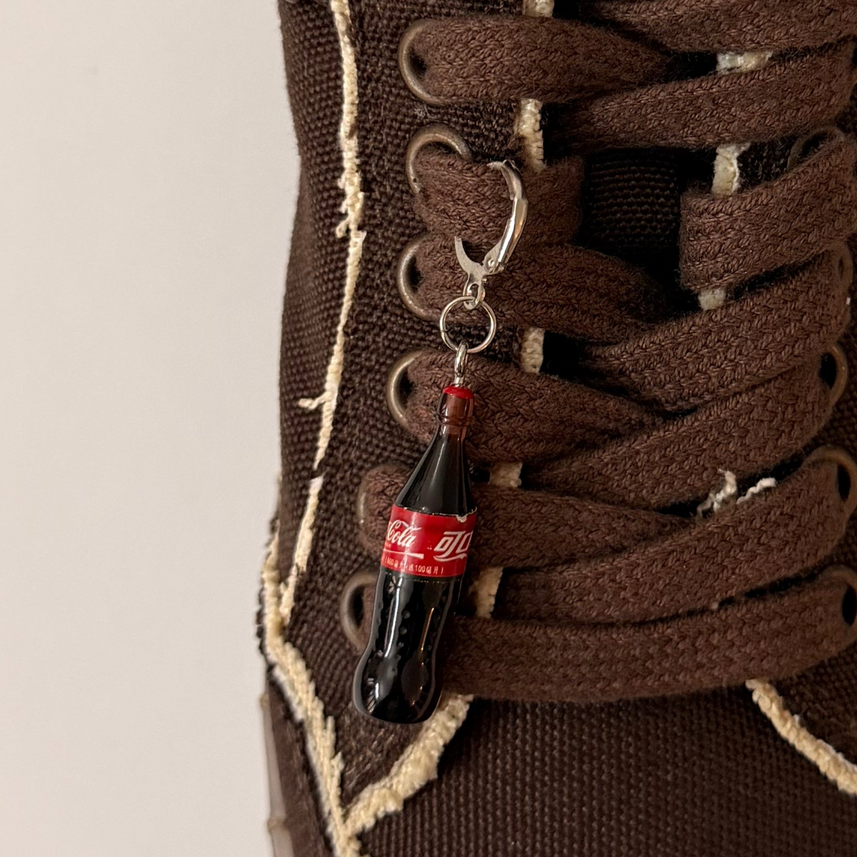 Coke Bottle Shoe Charm, mini Coca-Cola glass bottle charm on the laces of a brown canvas sneaker