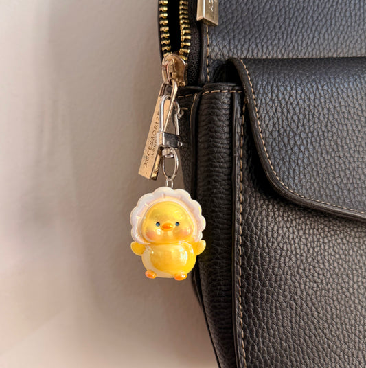 Duckie boo, a yellow duck in a white ruffle collar clipped to a black leather handbag zip.