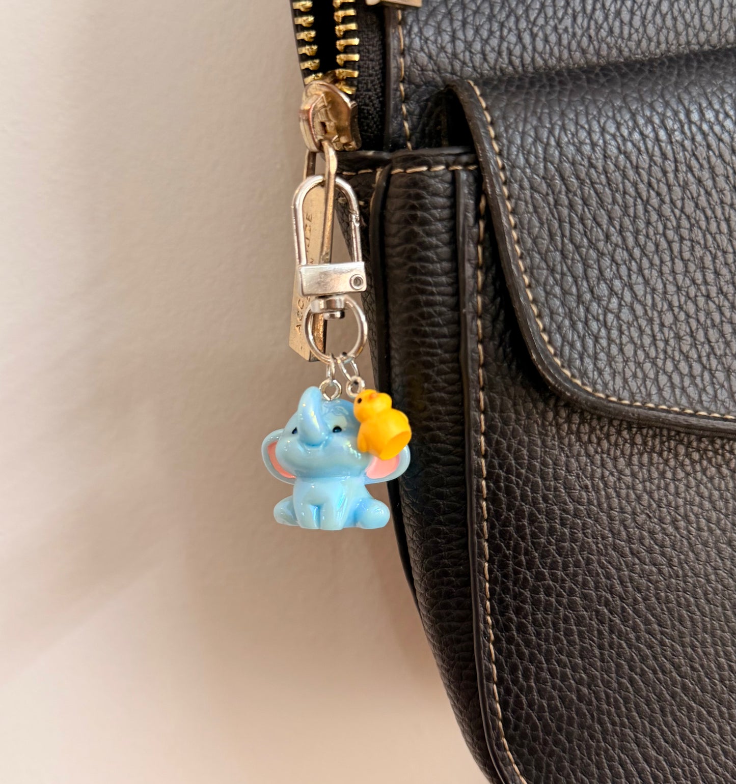 Ducky and Dumbo, a blue baby elephant with a yellow duckling on its trunk clipped to a black leather handbag zip.