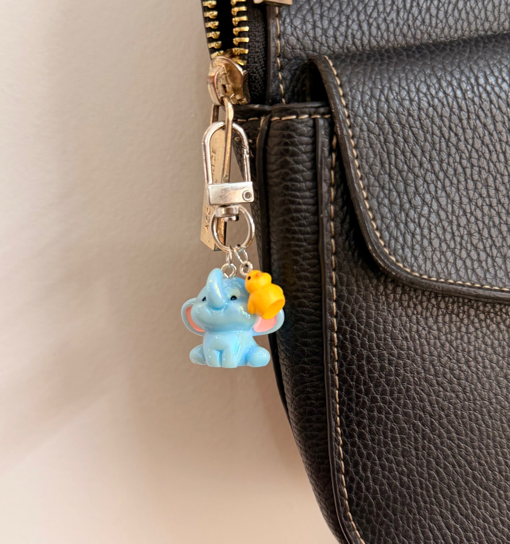 Ducky and Dumbo, a blue baby elephant with a yellow duckling on its trunk clipped to a black leather handbag zip.