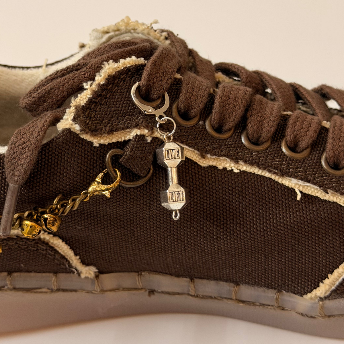 Dumbbell Shoe Charm, silver LIVE LIFT dumbbell charm on the laces of a brown canvas sneaker