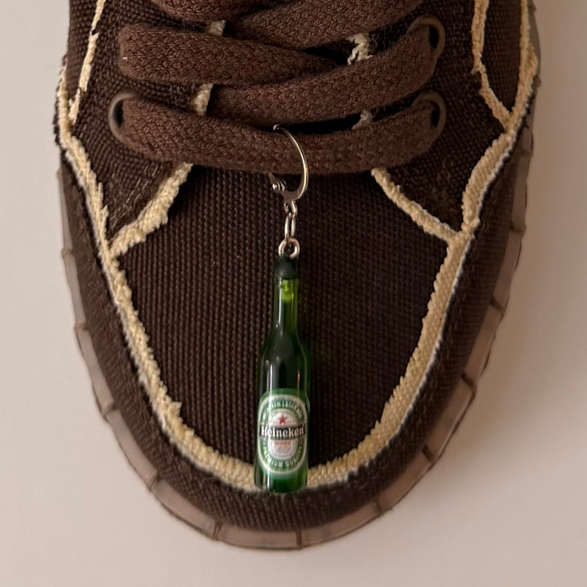 Heineken Shoe Charm, mini green Heineken beer bottle charm on the laces of a brown canvas sneaker