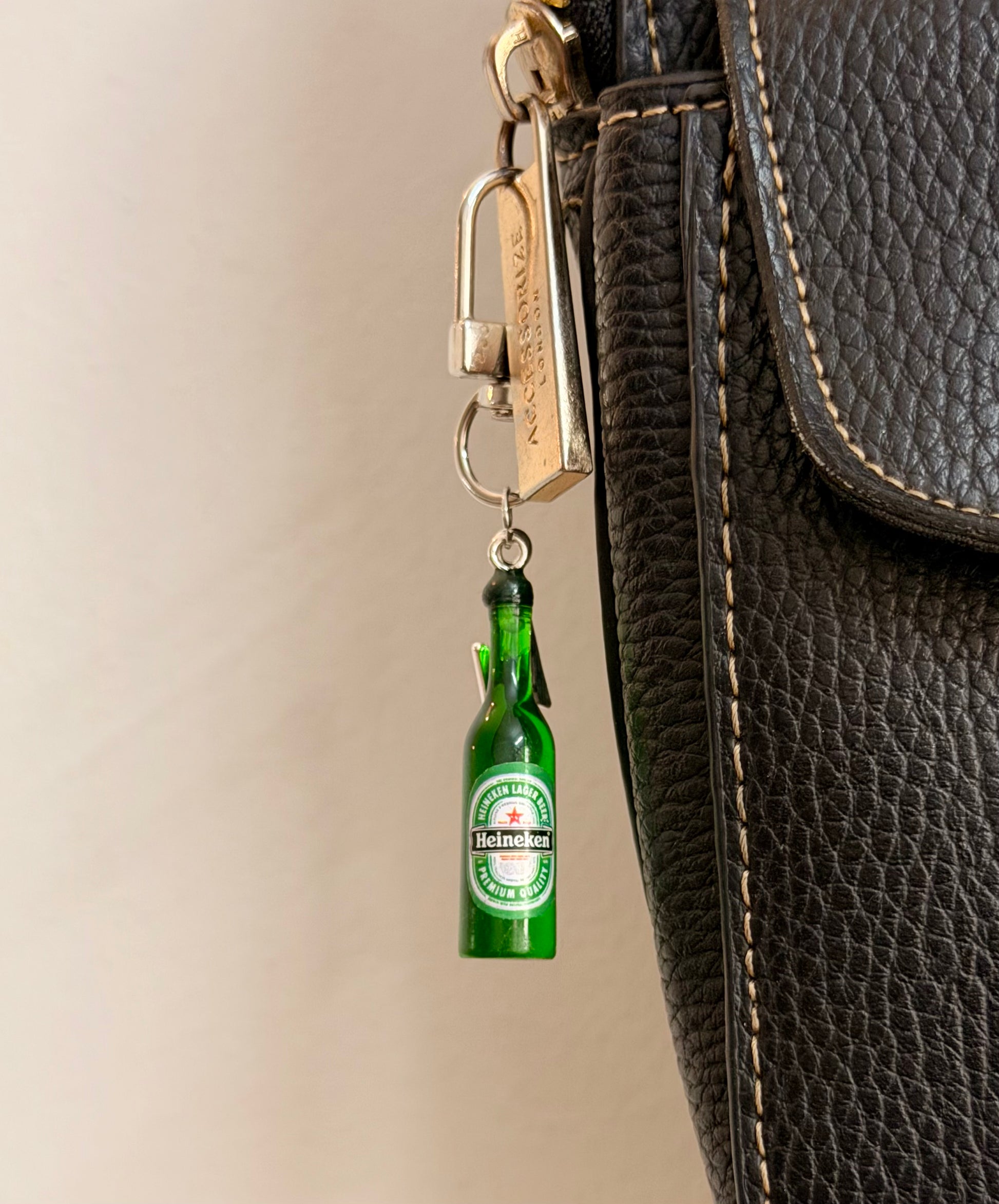 Heineken with Thunderbolt, a miniature green beer bottle with a silver thunderbolt charm clipped to a black leather handbag zip.