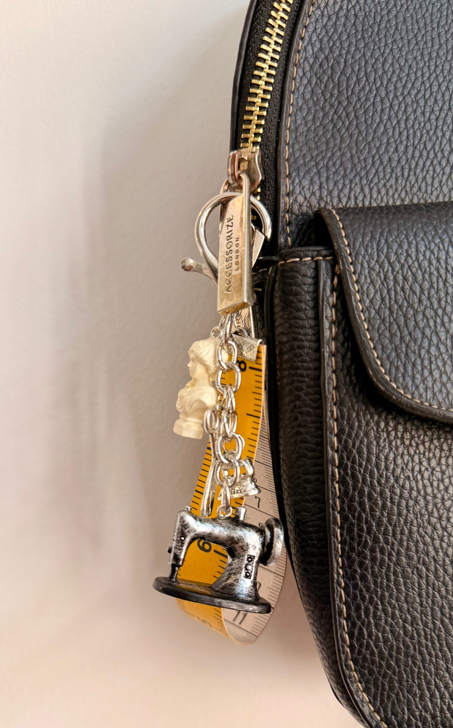 Couture Chaos Bag Charm, a sewing machine, scissors, an iron, a sculpture bust and a measuring tape on a silver chain shown from another angle.