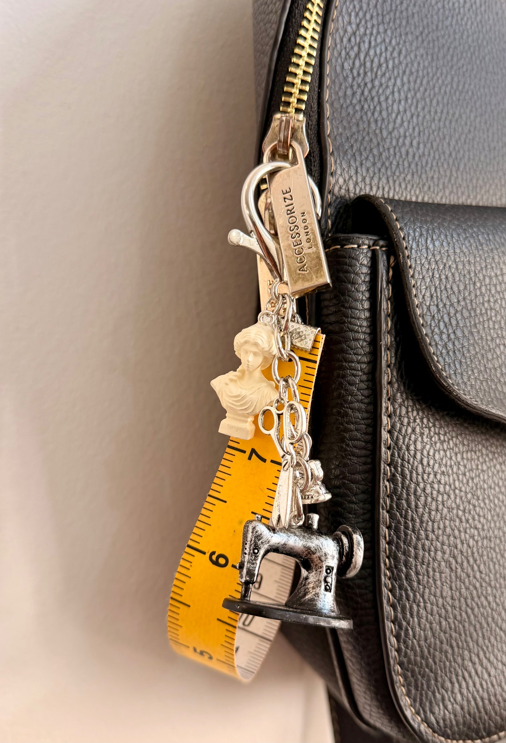 Couture Chaos Bag Charm, a sewing machine, scissors, an iron, a sculpture bust and a measuring tape on a silver chain shown from another angle.