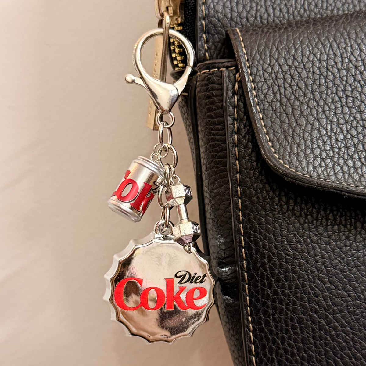 Pop the Cap, an oversized silver Diet Coke bottle cap with a miniature can and a silver dumbbell charm.