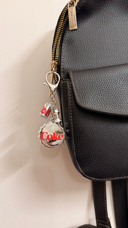 Pop the Cap, an oversized silver Diet Coke bottle cap with a miniature can and a silver dumbbell charm shown from another angle.