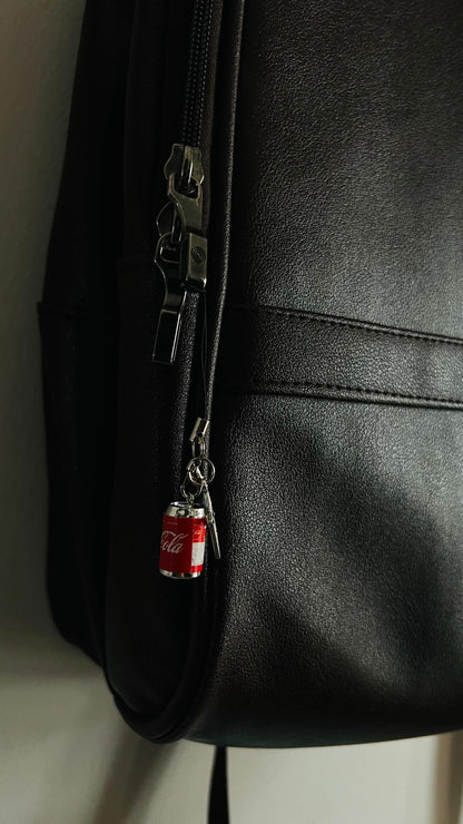 Red Coca-Cola can charm clipped to a black bag zipper