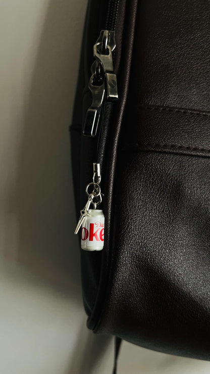 White Diet Coke can charm with silver star pendant hanging on a black bag zip