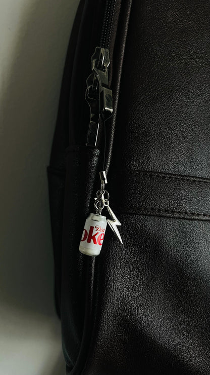 White Diet Coke can charm with silver thunderbolt clipped to a black bag zipper
