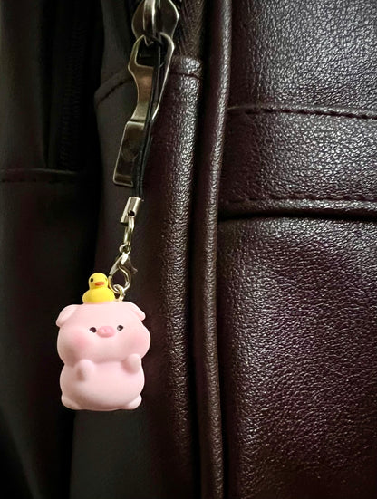 Pink piggy figurine bag charm with tiny yellow duck on its head, clipped to a dark brown bag