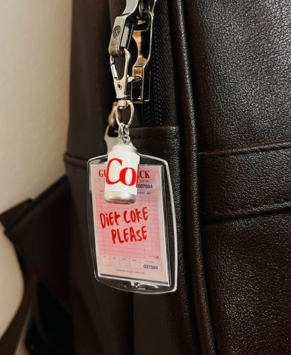 Pink guest check acrylic charm reading Diet Coke Please with white Diet Coke can on a brown bag