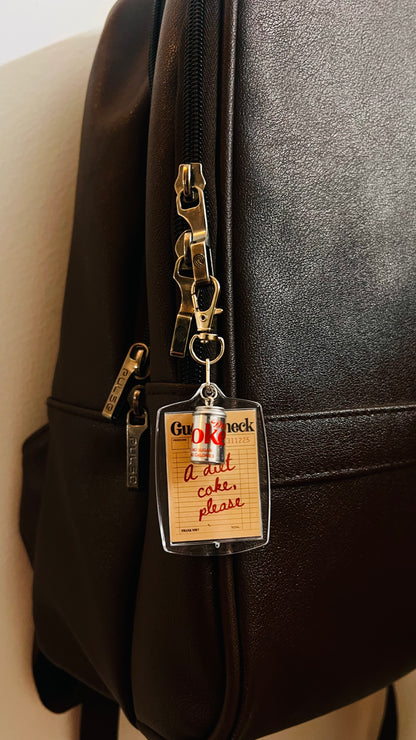 Guest check acrylic keychain with handwritten A diet coke, please note and mini Diet Coke can on a brown backpack