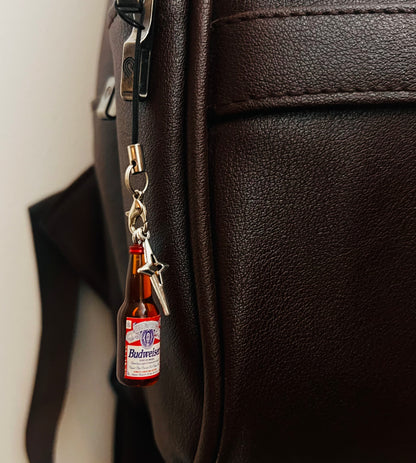 Budweiser beer bottle charm with star pendant on a black strap, close-up on a brown bag