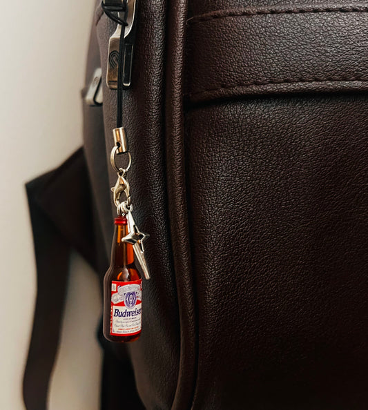 Budweiser beer bottle charm with star pendant on a black strap, close-up on a brown bag