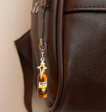 Corona Extra bottle charm with star pendant on a black phone strap against a brown bag