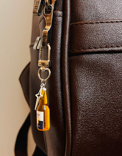 Corona bottle charm with star pendant hanging from a silver clasp on a dark brown bag