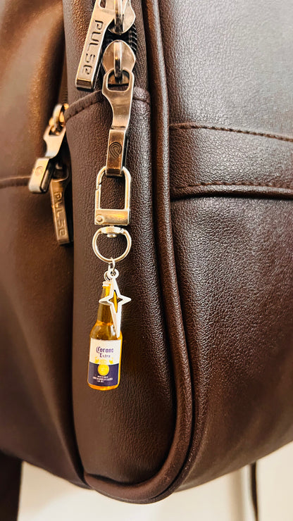 Corona Extra bottle charm with star pendant clipped to a dark brown backpack zipper