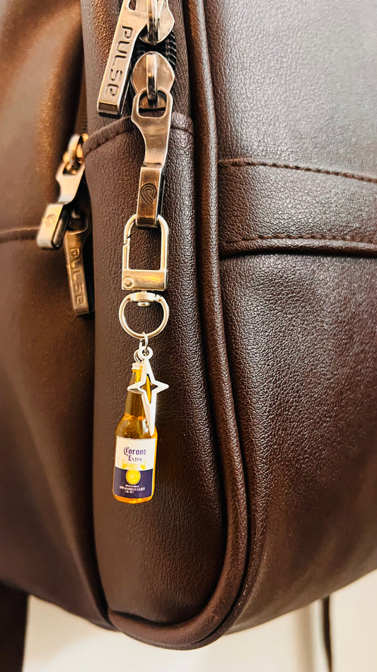 Corona Extra bottle charm with star pendant clipped to a dark brown backpack zipper